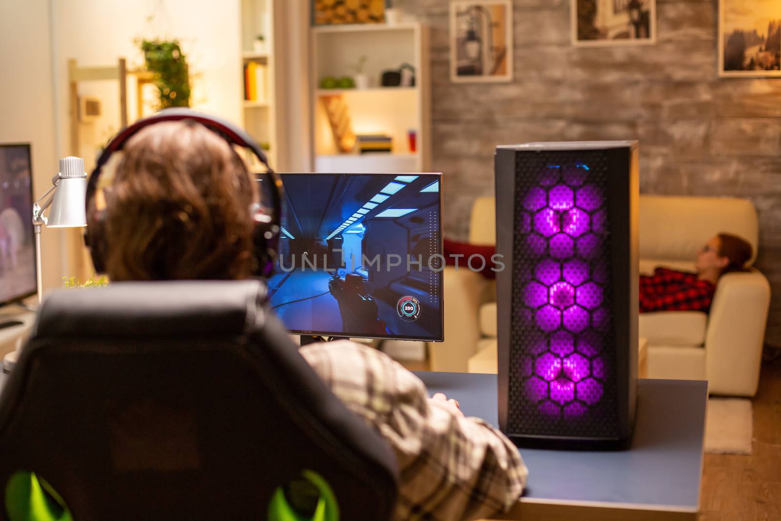 Back view of gamer male playing a shooter on his powerful PC computer late at night in the living room.