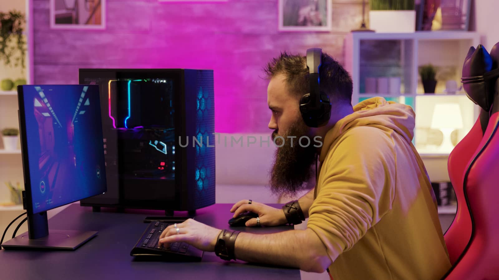 Professional game player wearing headphones in a room with colorful neons while playing online video games.