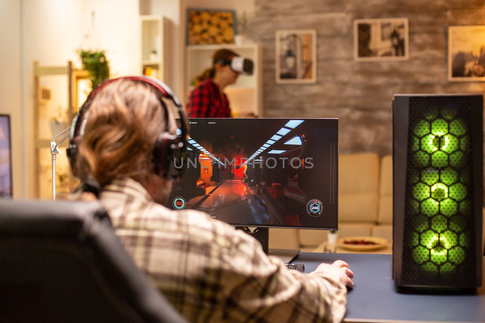 Back view of professional video gamer playing on powerful PC late at night in the living room.