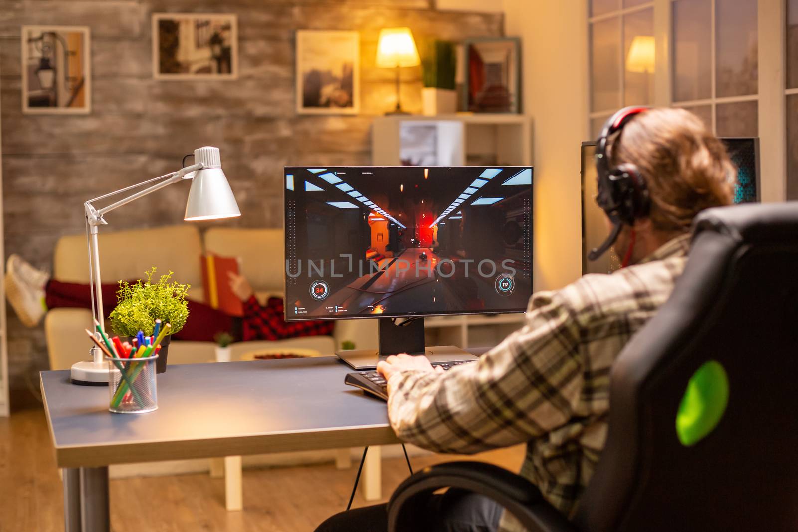 Back view of gamer male playing a shooter on his powerful PC computer late at night in the living room.