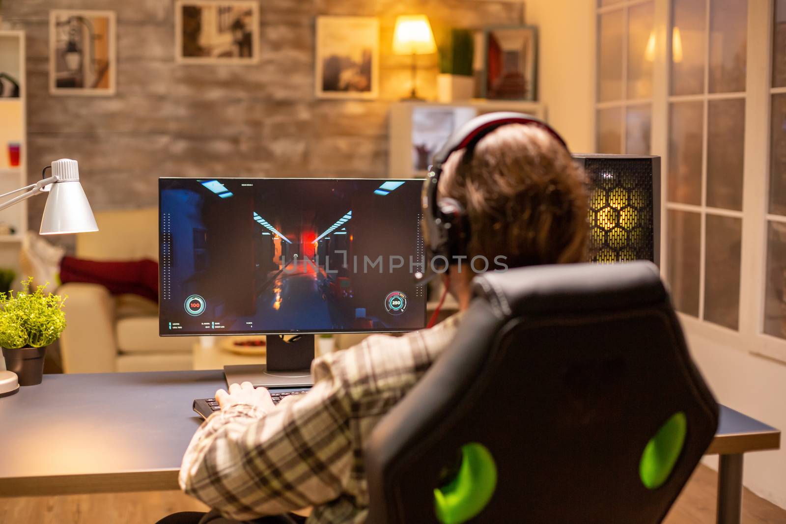 Back view of gamer male playing a shooter on his powerful PC computer late at night in the living room.