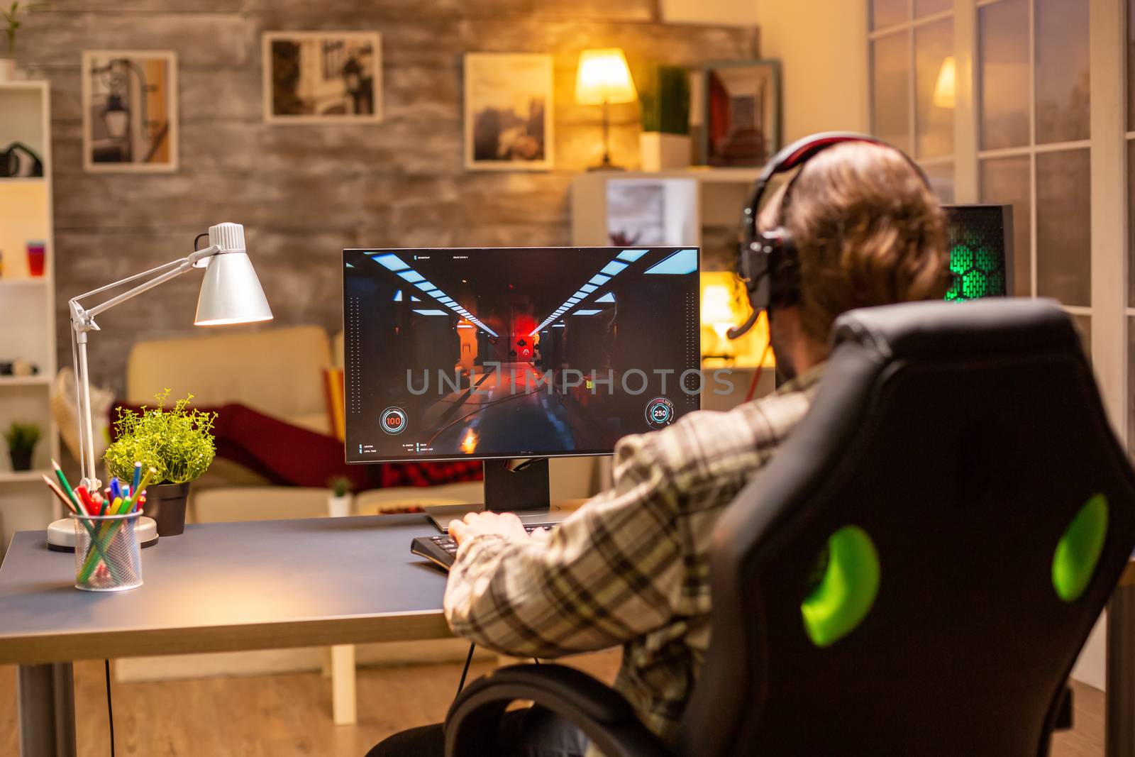 Back view of gamer male playing a shooter on his powerful PC computer late at night in the living room.