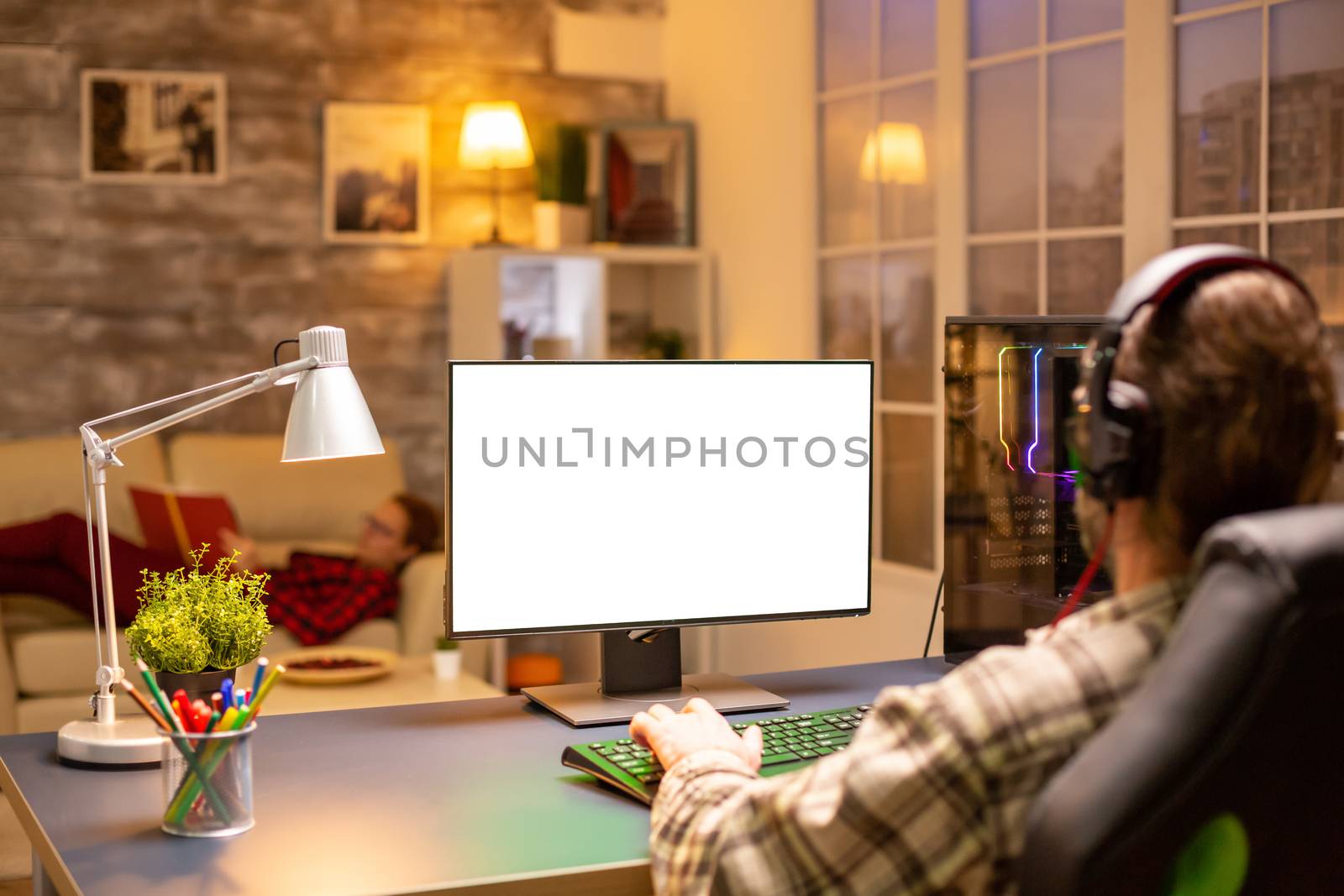 Back view of professional gamer looking at computer with isolated mock up screen late at night in the living room