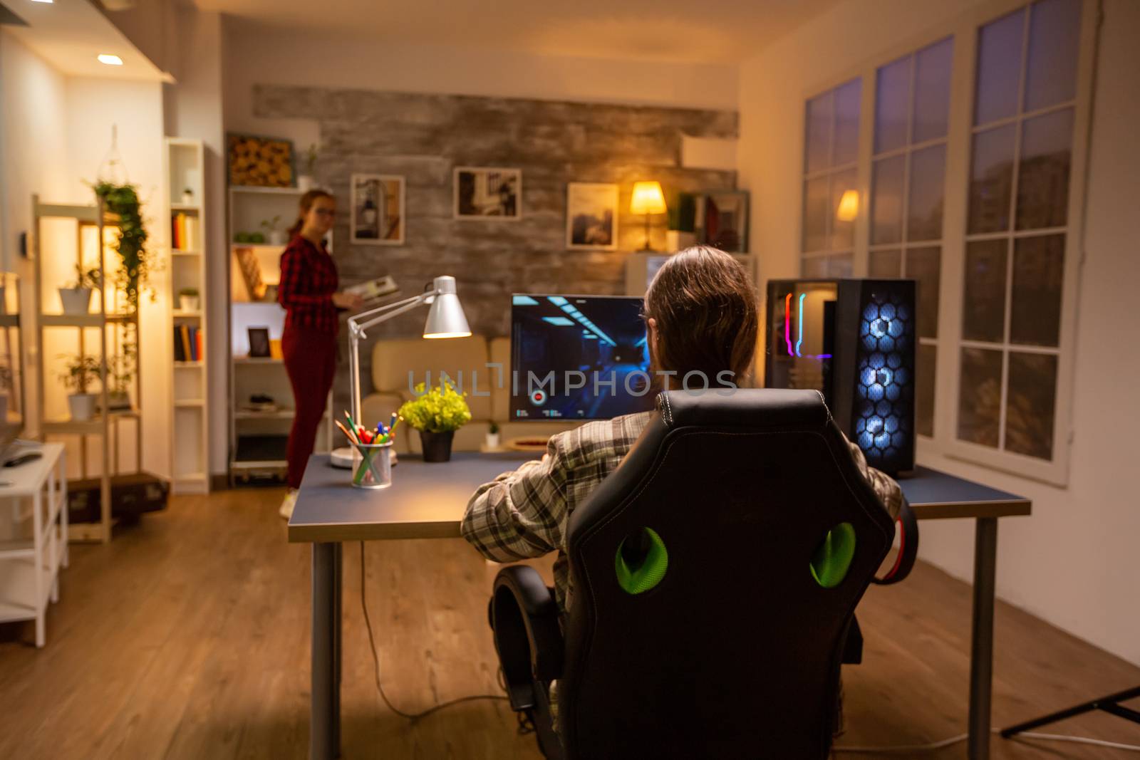 Back view of professional video gamer playing on powerful PC late at night in the living room.