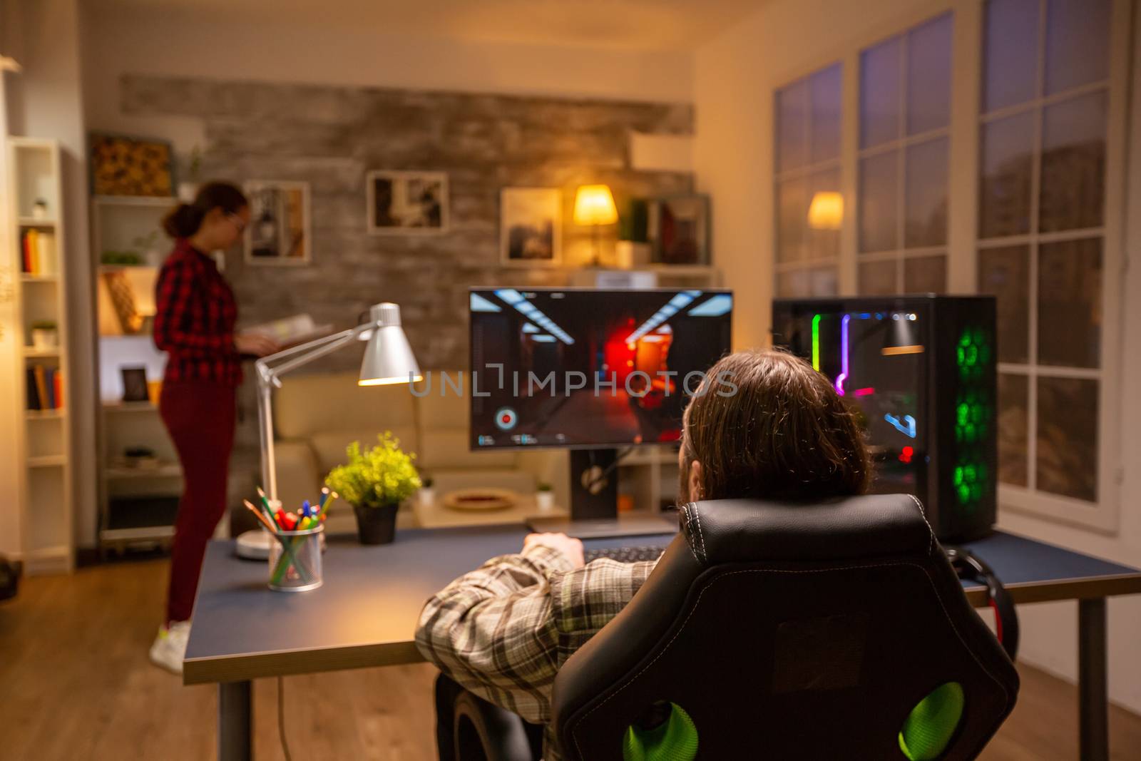 Back view of professional video gamer playing on powerful PC late at night in the living room.