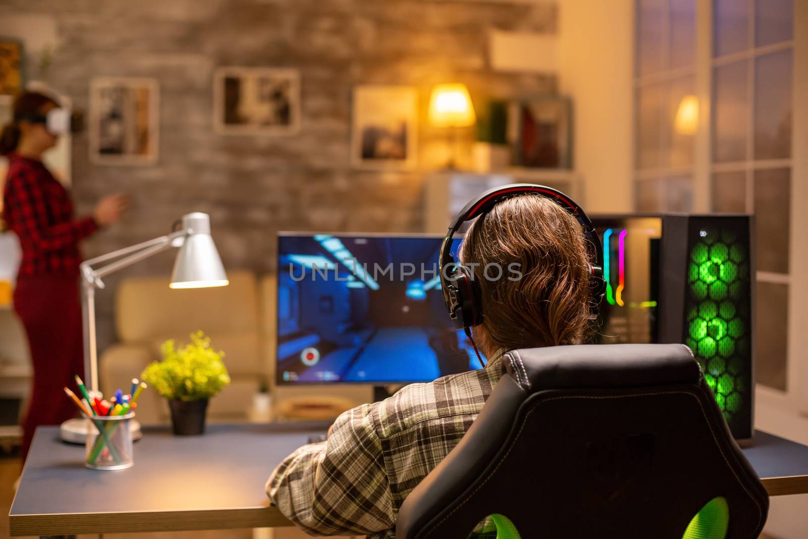 Back view of professional video gamer playing on powerful PC late at night in the living room.