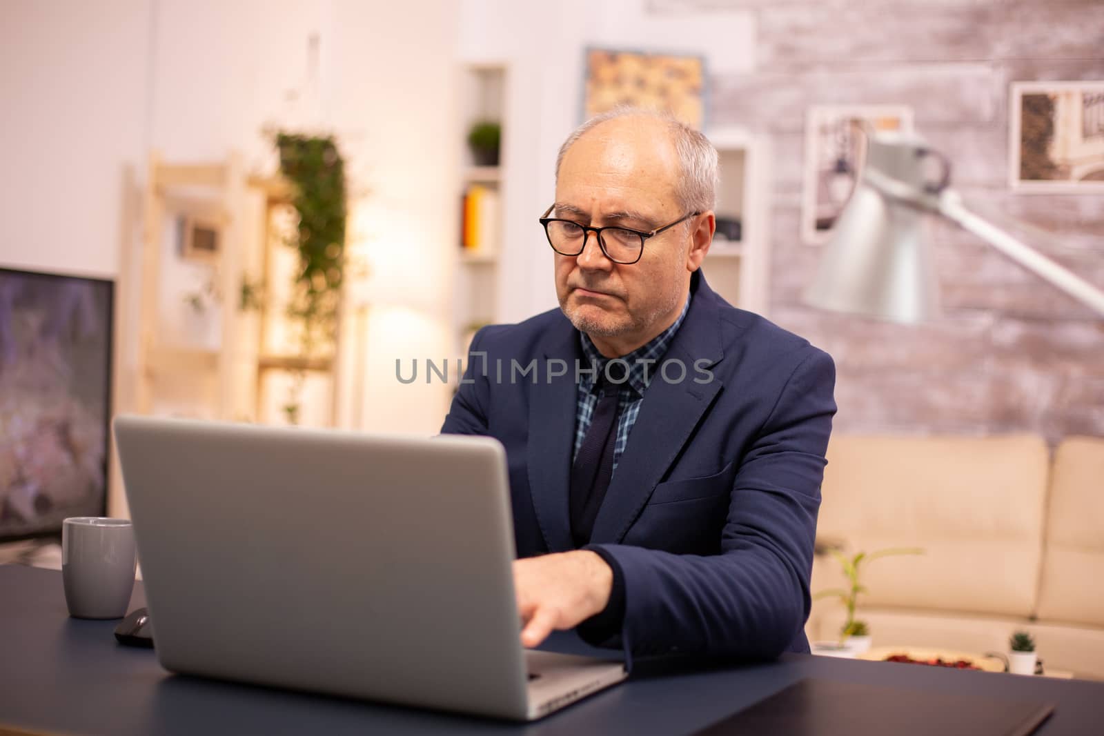 Elderly man typing on laptop in cozy living room.