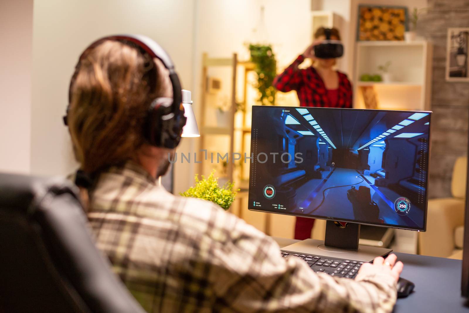 Back view of professional video gamer playing on powerful PC late at night in the living room.