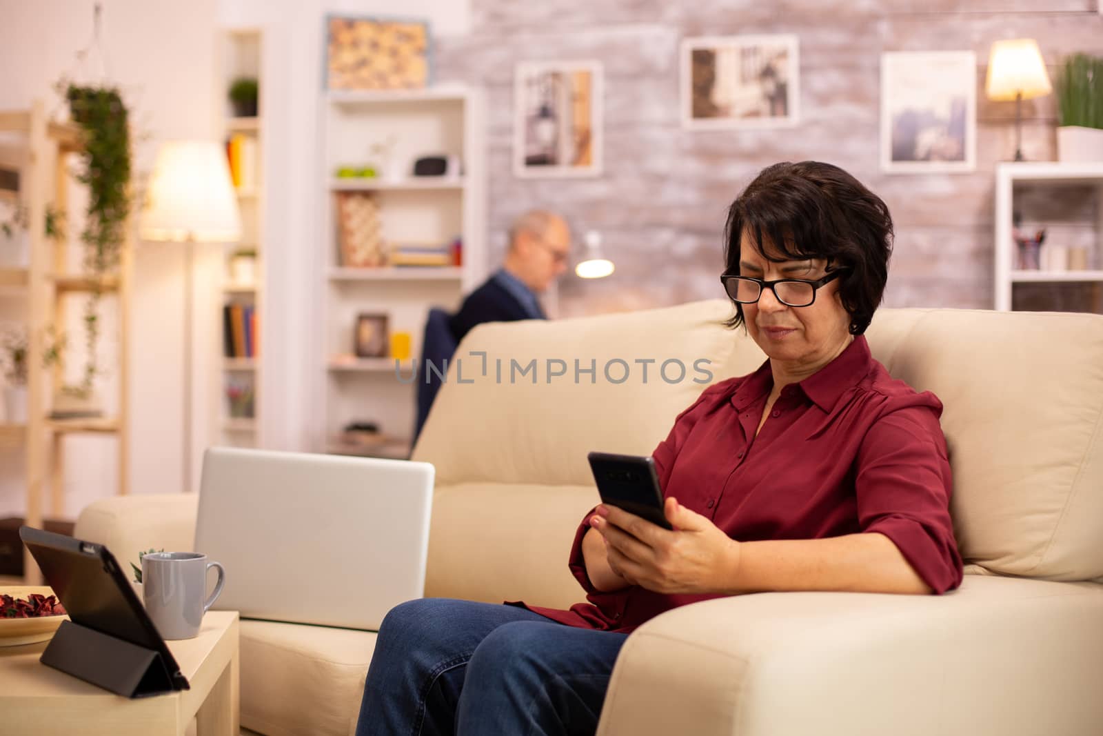 Elderly lady using modern technology in her house. She has a modern smartphone in her hands