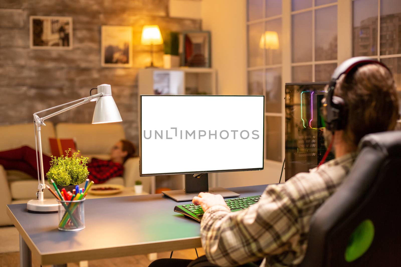 Back view of professional gamer looking at computer with isolated mock up screen late at night in the living room