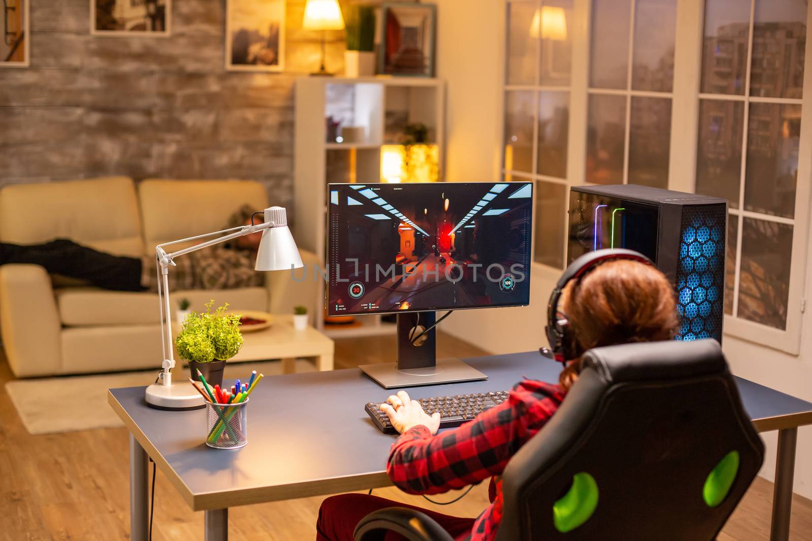 Back view of female gamer playing on powerful computer PC late at night in the living room.