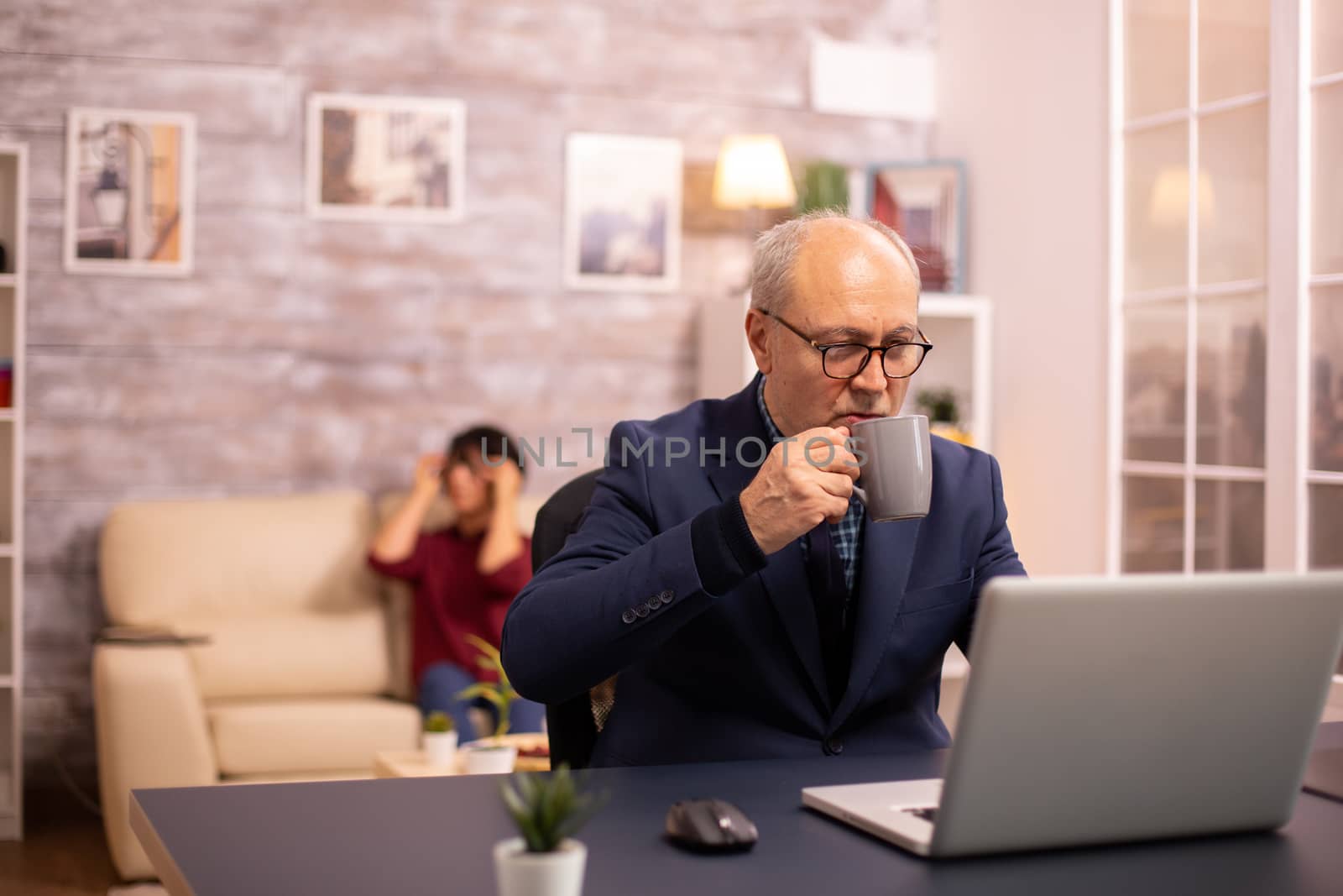 Elderly man sips coffee while working on a latop in modern cozy living room