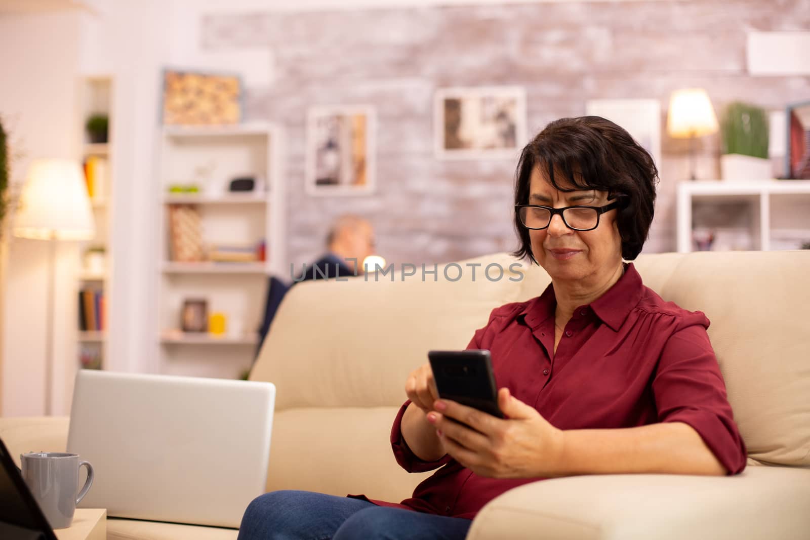 Elderly lady using modern technology in her house. She has a modern smartphone in her hands