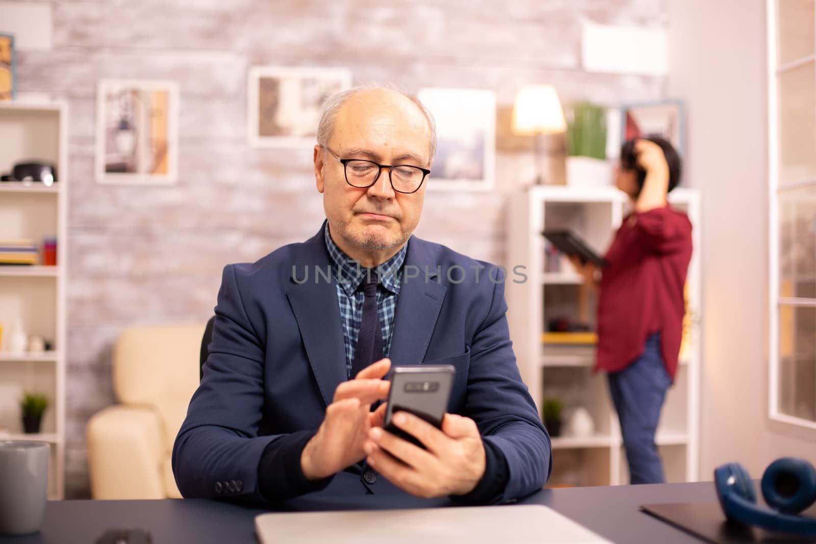 Old man using new technology in cozy house. He has a smartphone in his hands