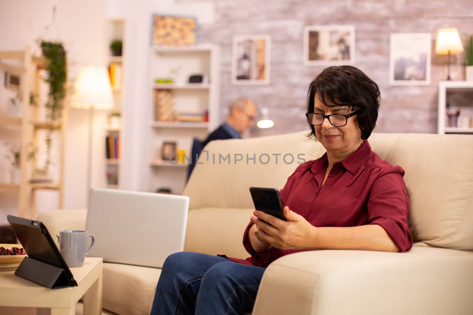 Elderly lady using modern technology in her house. She has a modern smartphone in her hands