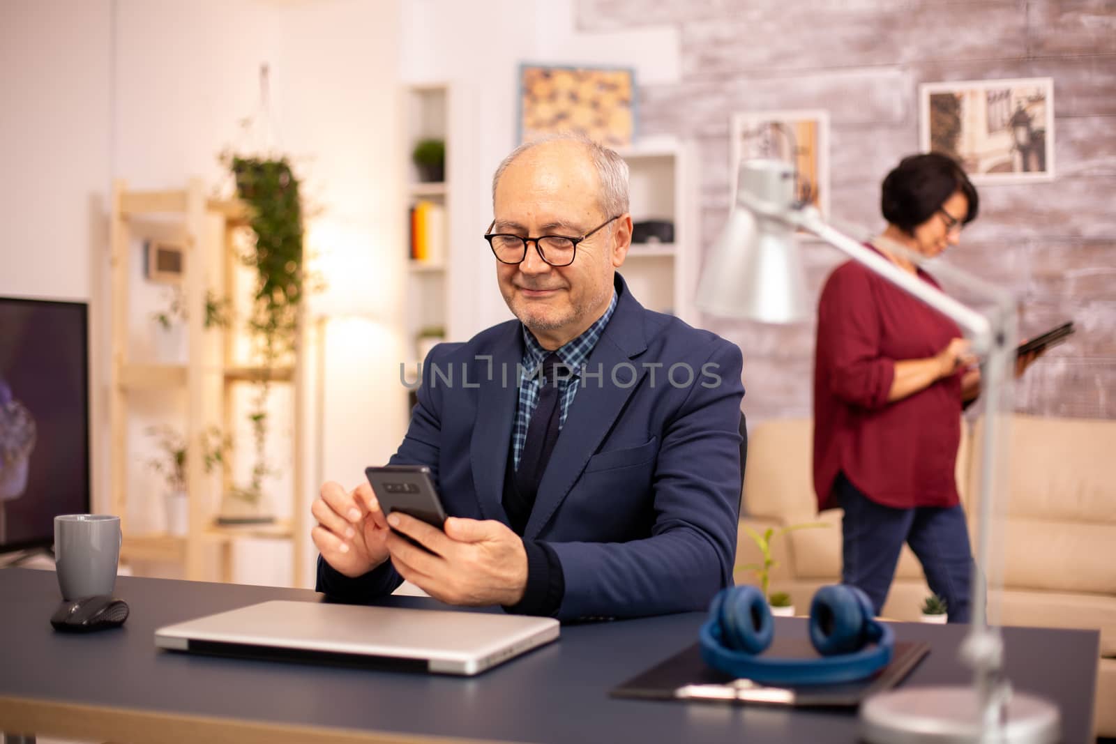 Old man using new technology in cozy house. He has a smartphone in his hands