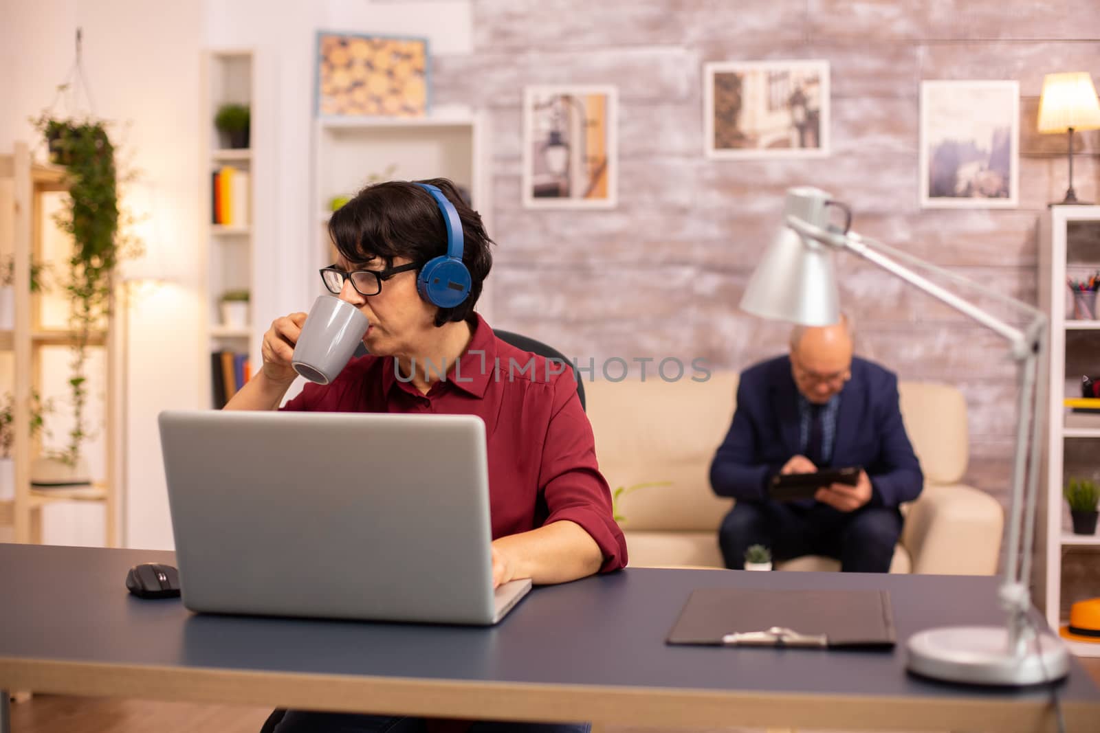 Concept photo of old lady using modern technology. He uses wirelles headphones and a laptop
