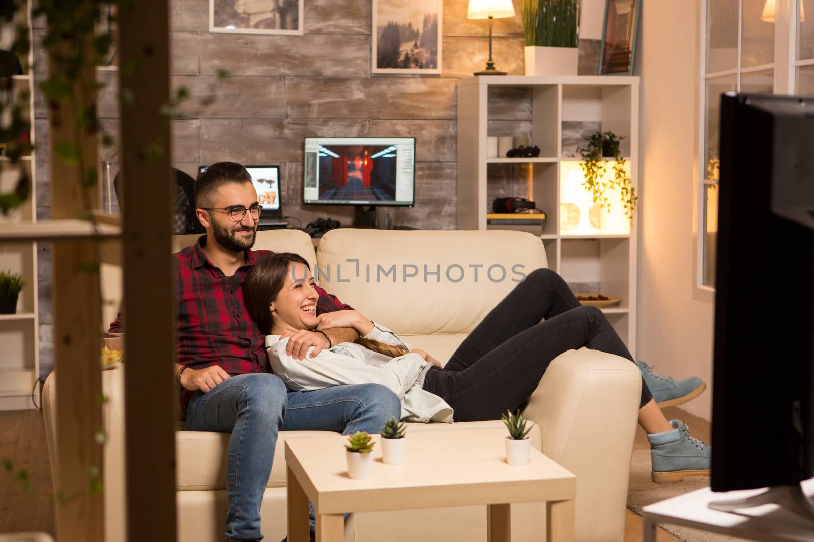 Lovely young couple relaxing on couch and watching a movie on tv at night
