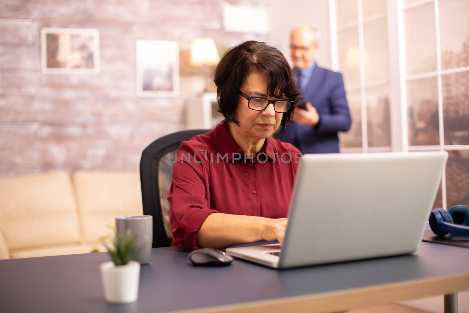 Old woman in her 60s using a modern laptop in her cozy house late in the evening