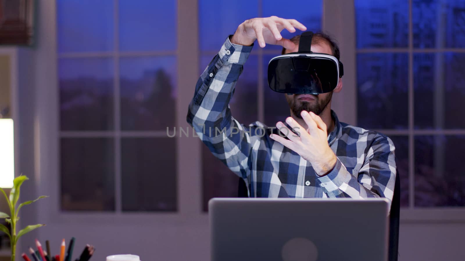 Young businessman using virtual reality goggles while working in home office during at night.