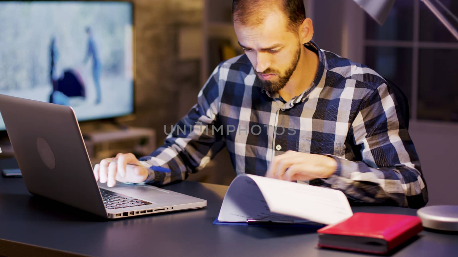 Young entrepreneur working on laptop and signing documents in home office during night hours.