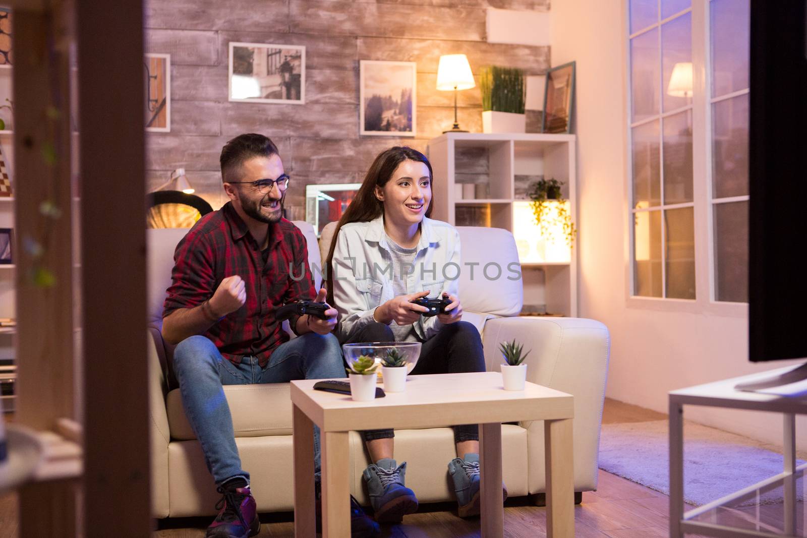 Happy young couple after winning at video games on television sitting on couch at night.