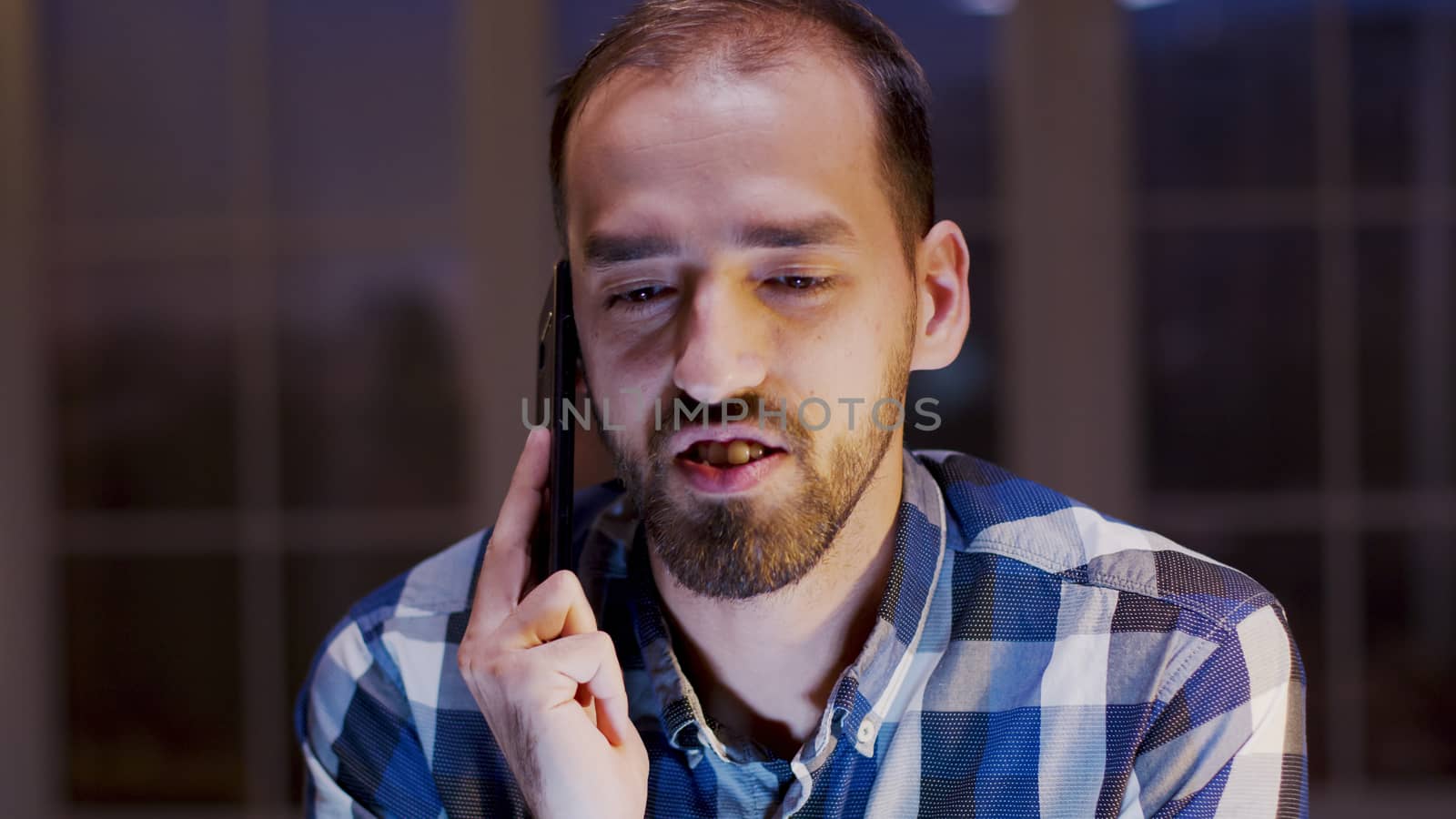 Caucasian entrepreneur having a business conversation on mobile phone. Businessman working during late night work hours in home office.