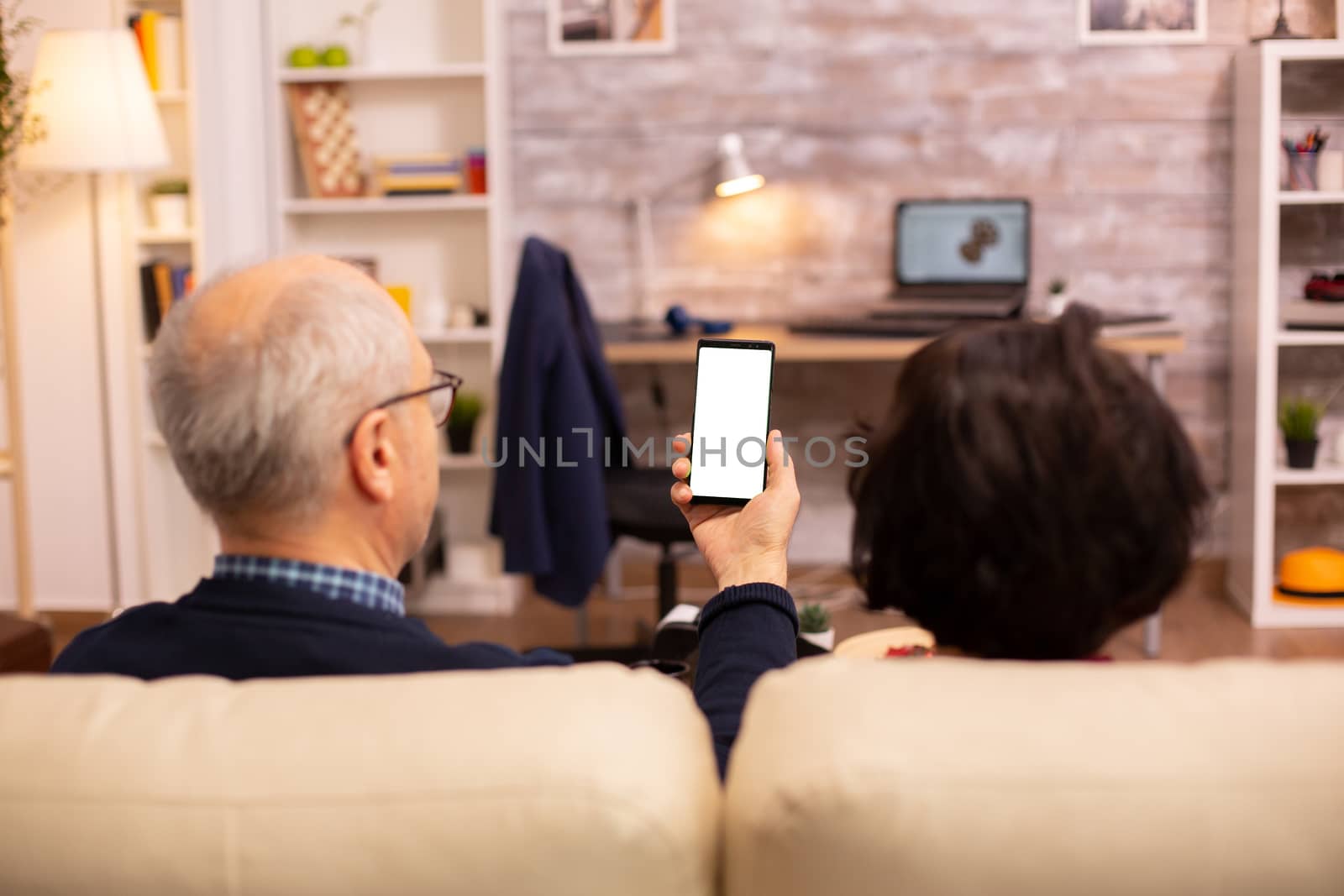 Back view of elderly retired couple looking at a smartphone with white isolated screen.