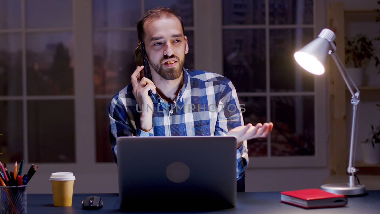 Businessman having an argument conversation over the phone while working in his home office during night hours.