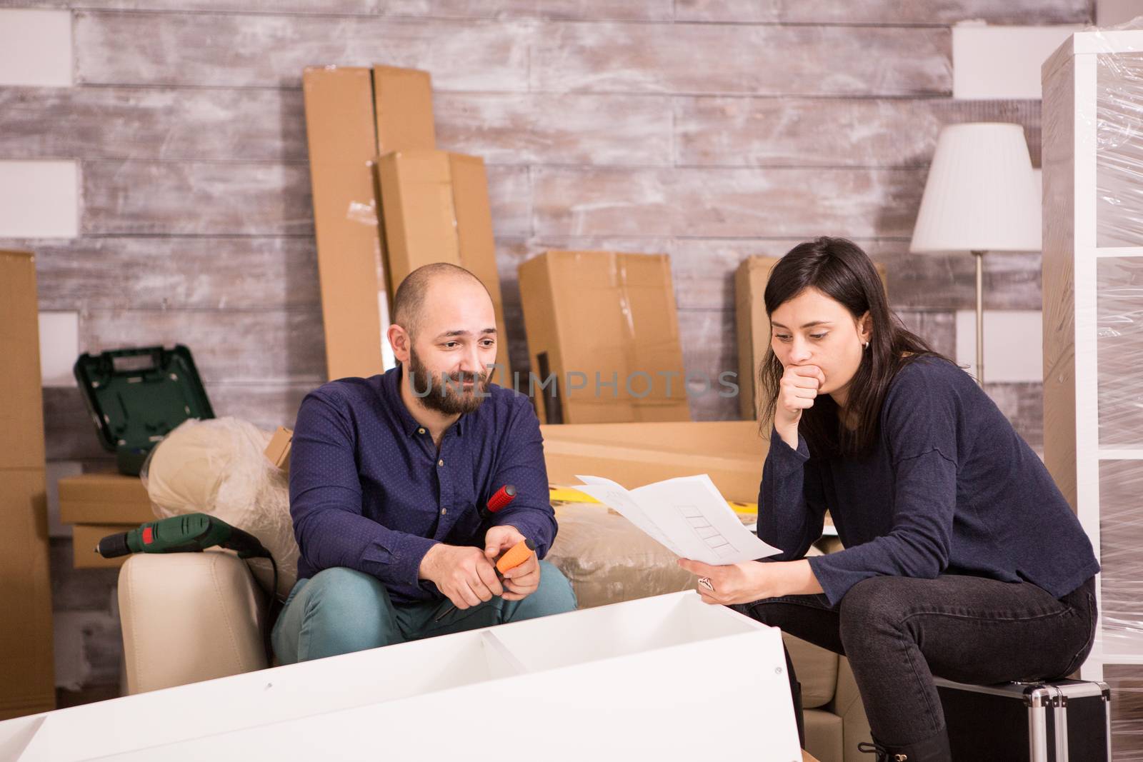 Caucasian young couple assembling furniture in new apartment. Girlfriend reading instructions.
