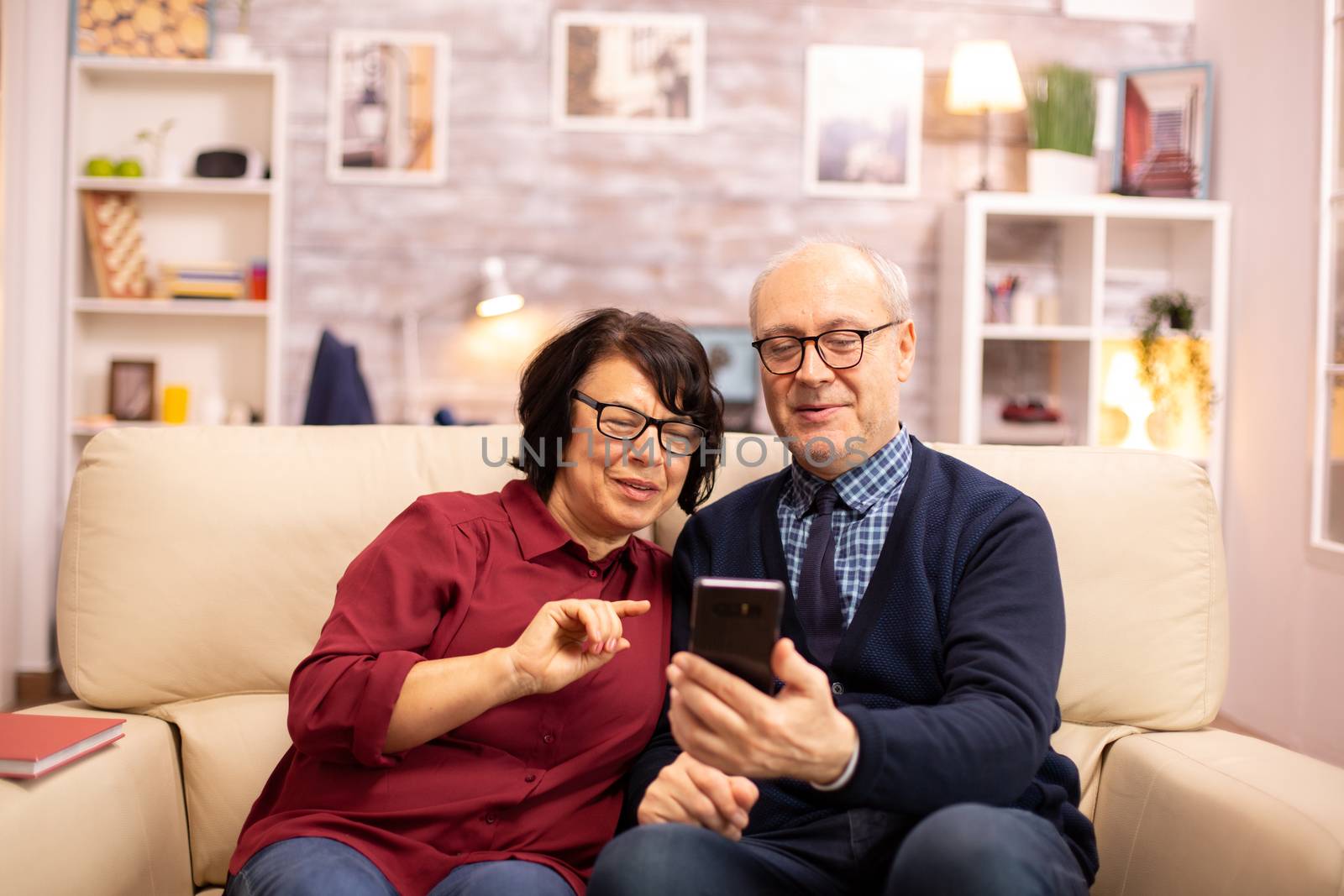 Beautiful elderly couple taking a selfie while sitting on the couch in the living room
