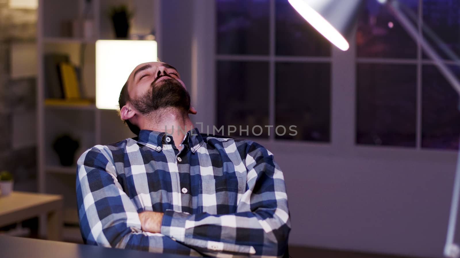 Tired young caucasian entrepreneur sleeping on chair in his home office. Overworked businessman.