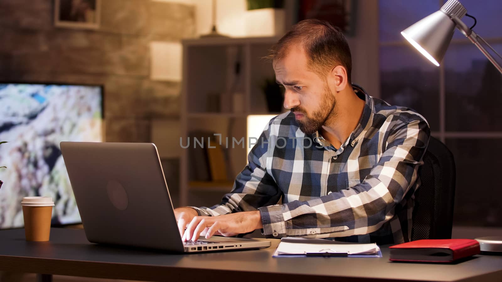 Businessman typing on laptop and searching through documents while working from home office.