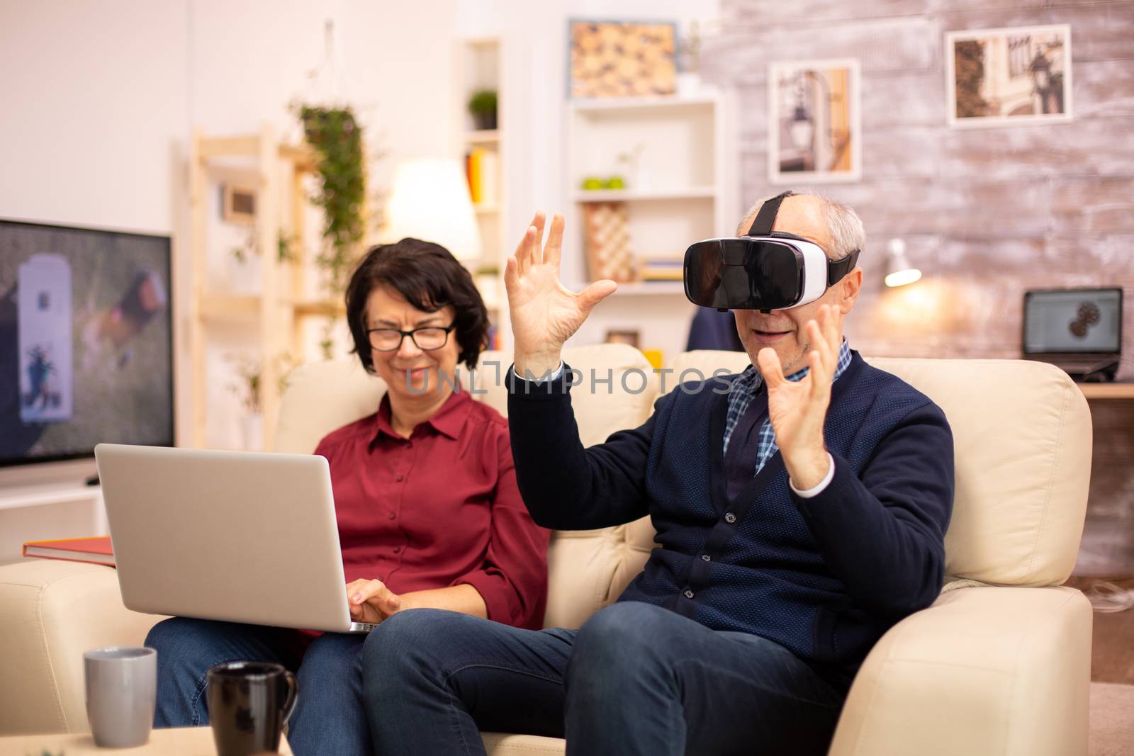 Old elderly retired man using VR virtual reality headset in their cozy apartment.