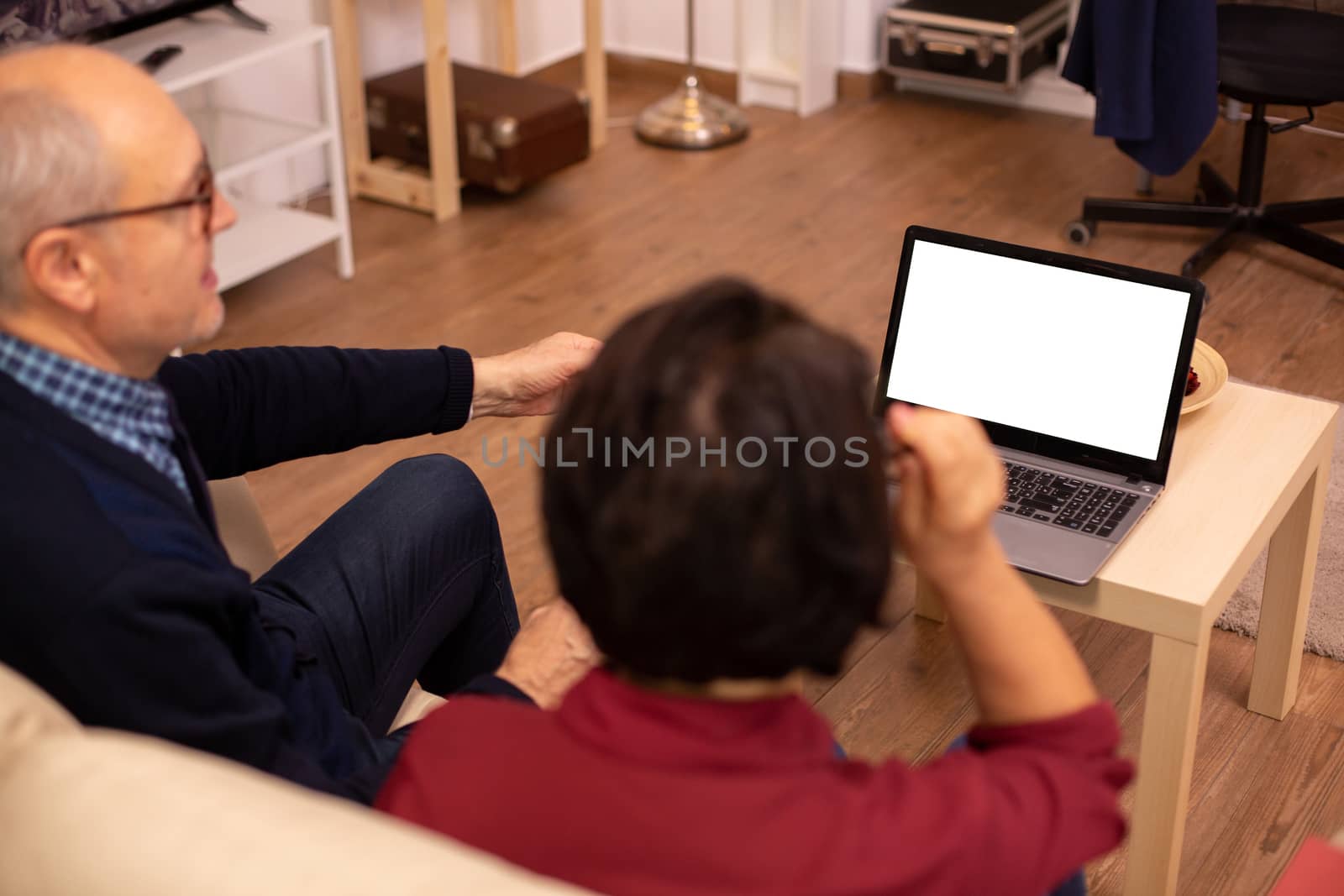 Back view of old couple in their living room looking a laptop with white isolated mock-up.