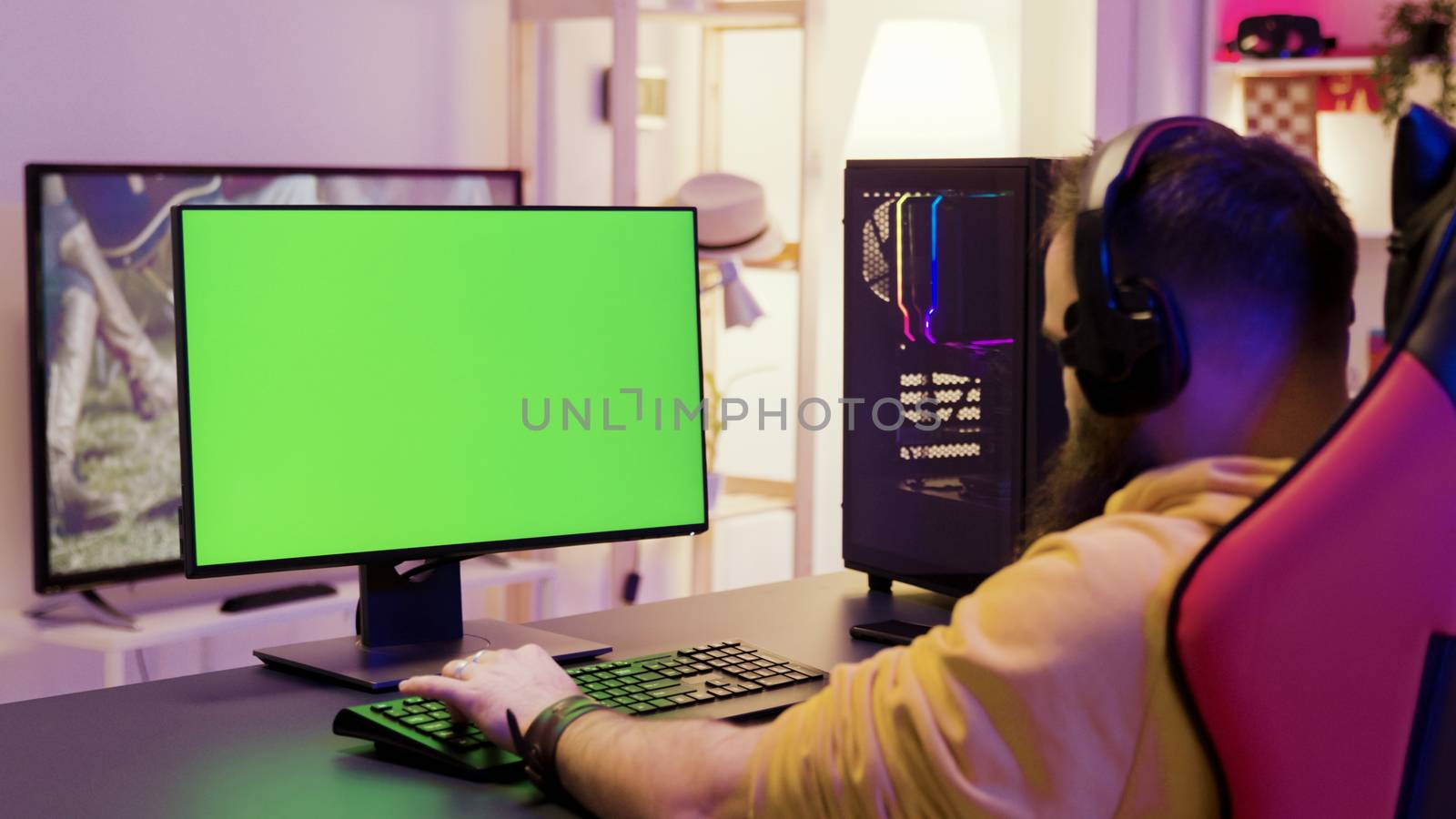 Over shoulder footage of man playing video games on computer with green screen. Professional game player.