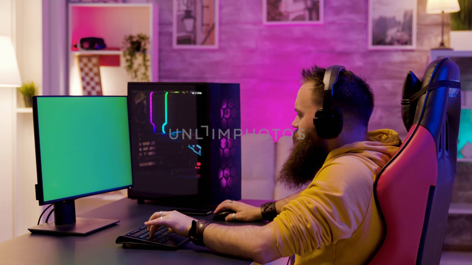 Man playing on powerfull gaming pc in a room with neon lights. Computer with green screen.