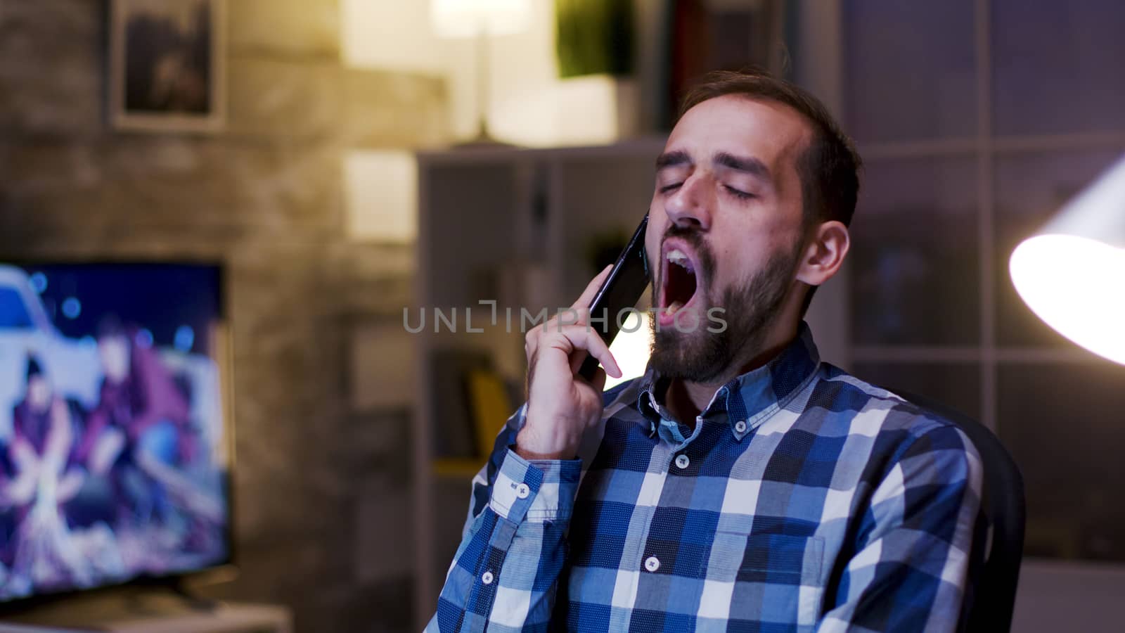 Overworked businessman yawn during a conversation on mobile phone. Businessman working in home office during late hours.