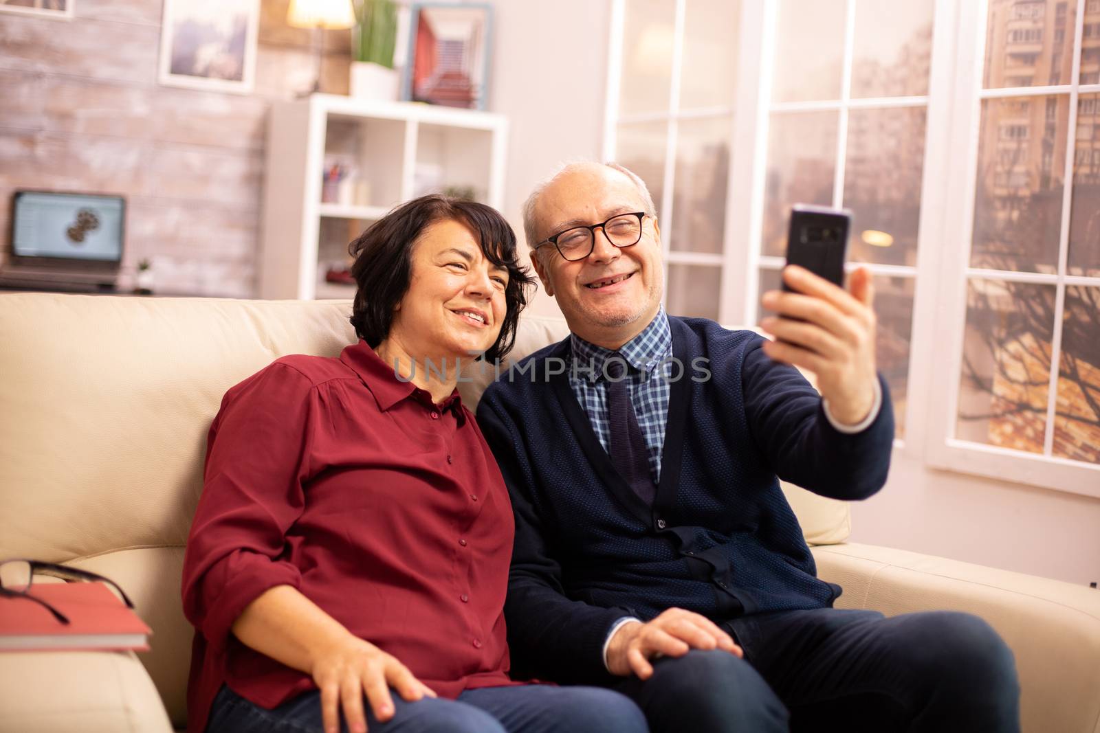 Beautiful elderly couple taking a selfie while sitting on the couch in the living room