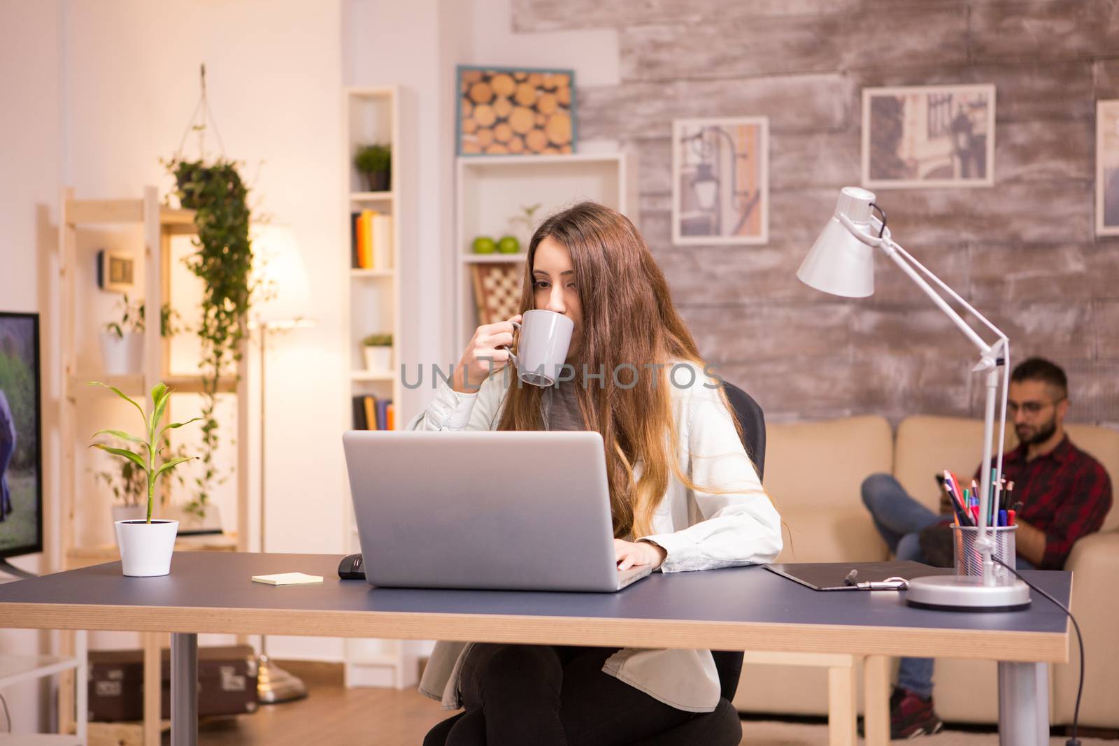 Girl taking a sip of coffee while working on laptop in home office by DCStudio