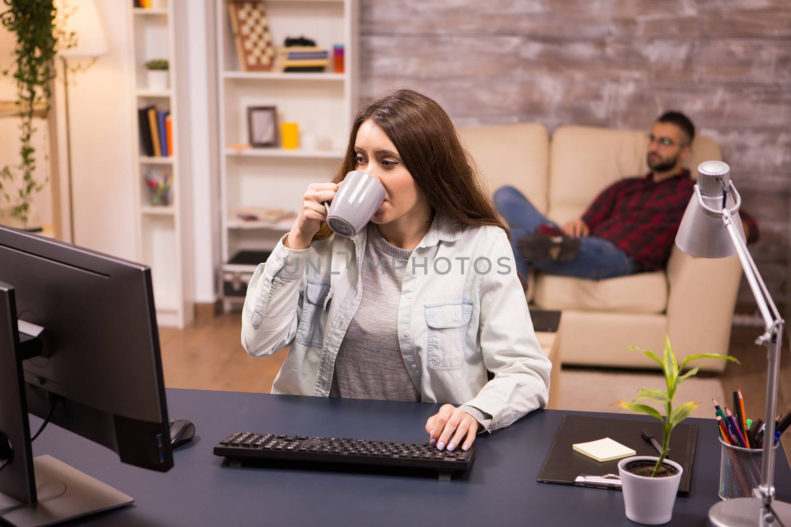 Caucasian female freelancer taking a sip of coffee while working on computer from home by DCStudio