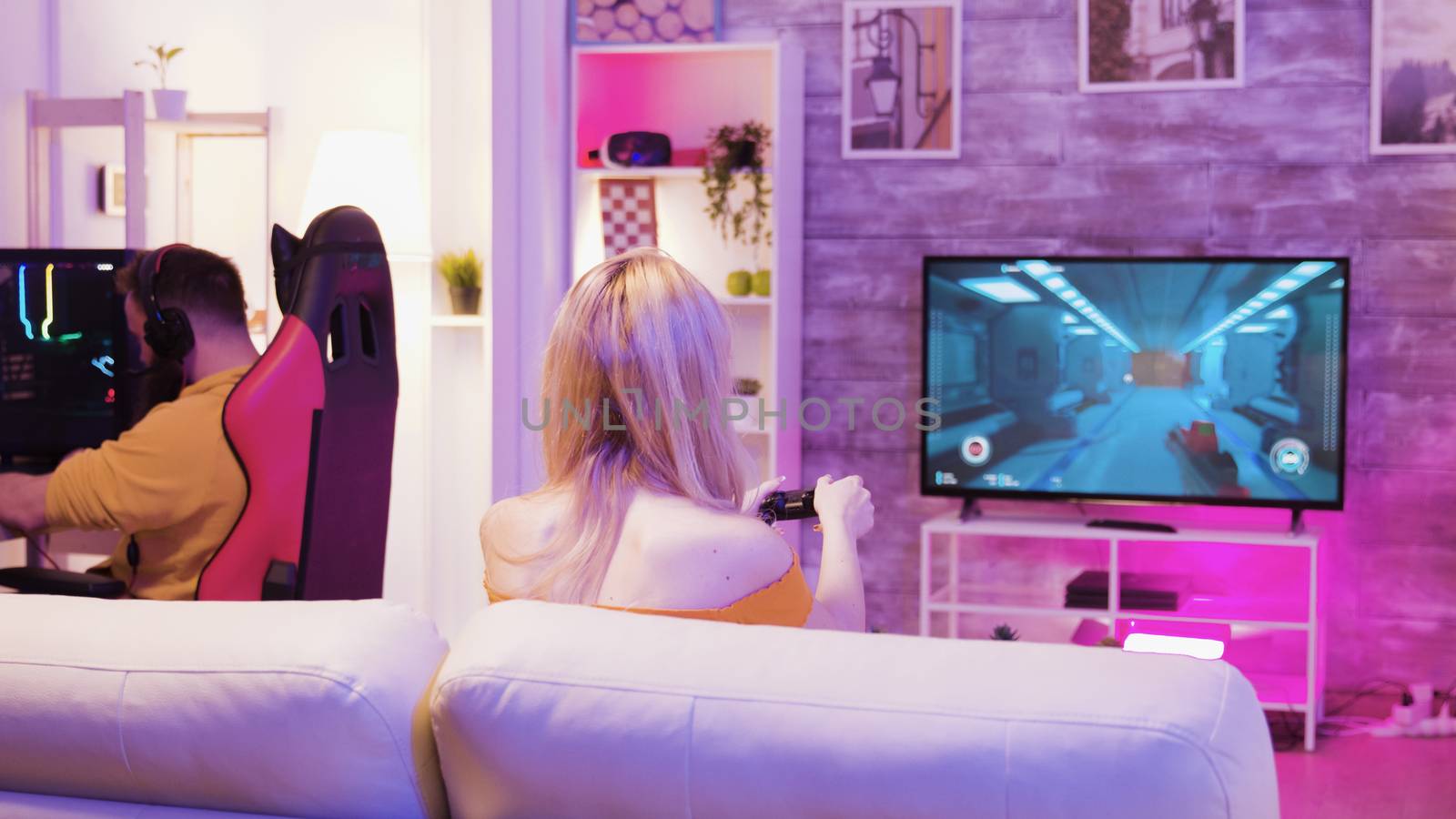 Beautiful young woman happy to win at online video games sitting on sofa using wireless controller. Boyfriend sitting on gaming chair.