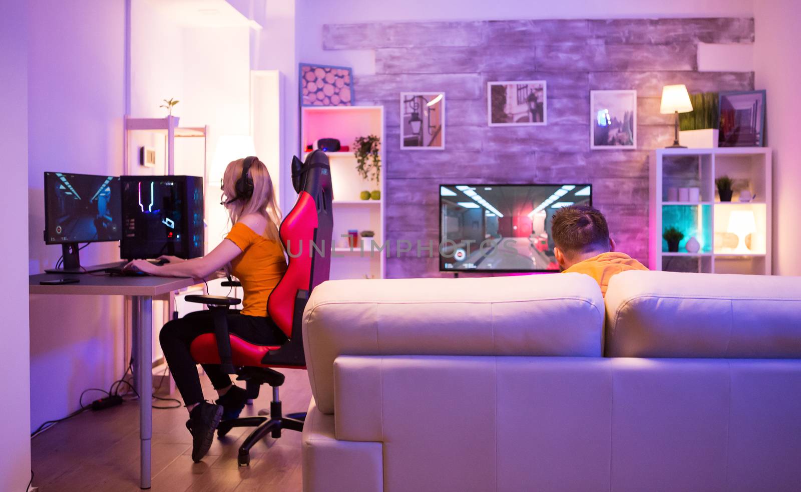 Back view of young man sitting on couch playing games. Girl sitting on gaming chair.