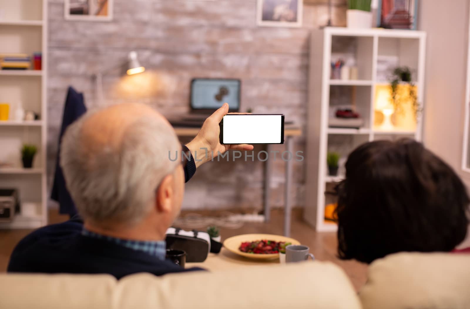 Back view of elderly retired couple looking at a smartphone with white isolated screen by DCStudio