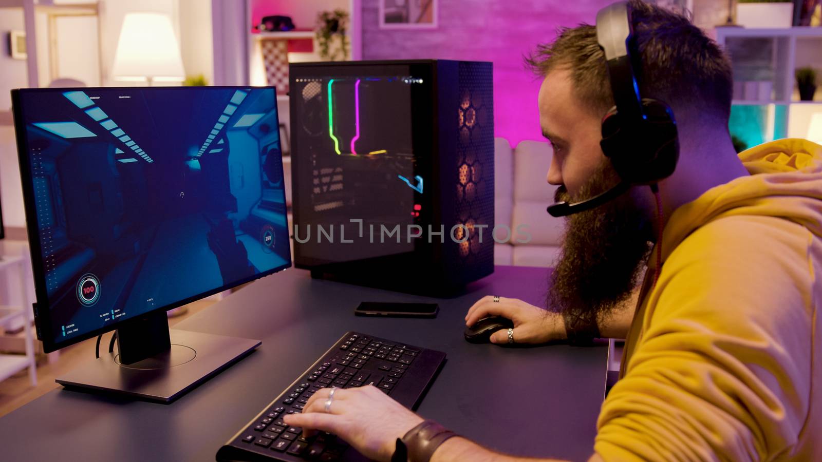 Hipster bearded man playing professional online games on his computer. Gamer in a room with colorful neon lights.