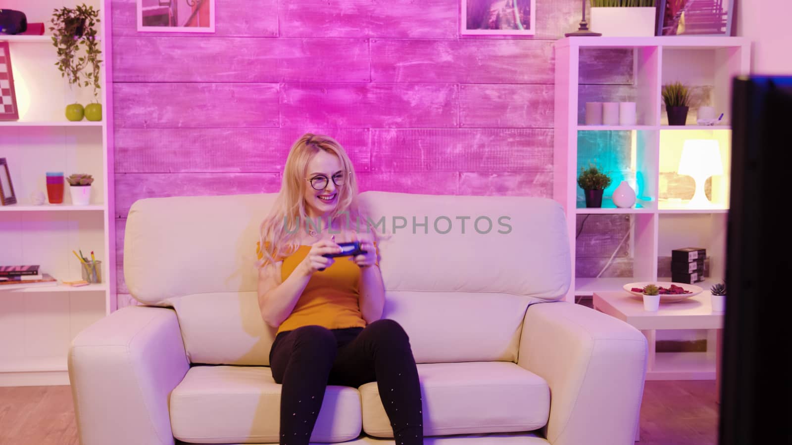 Beautiful blonde girl excited while playing video games using wireless controllers. Cheerful girl playing video games.