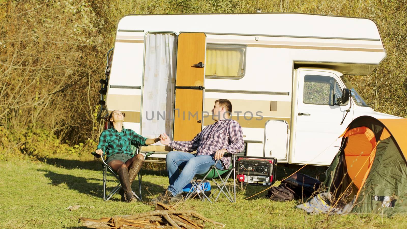 Relaxed couple setting up their camping chairs in front of their retro camper van. Camping tent.