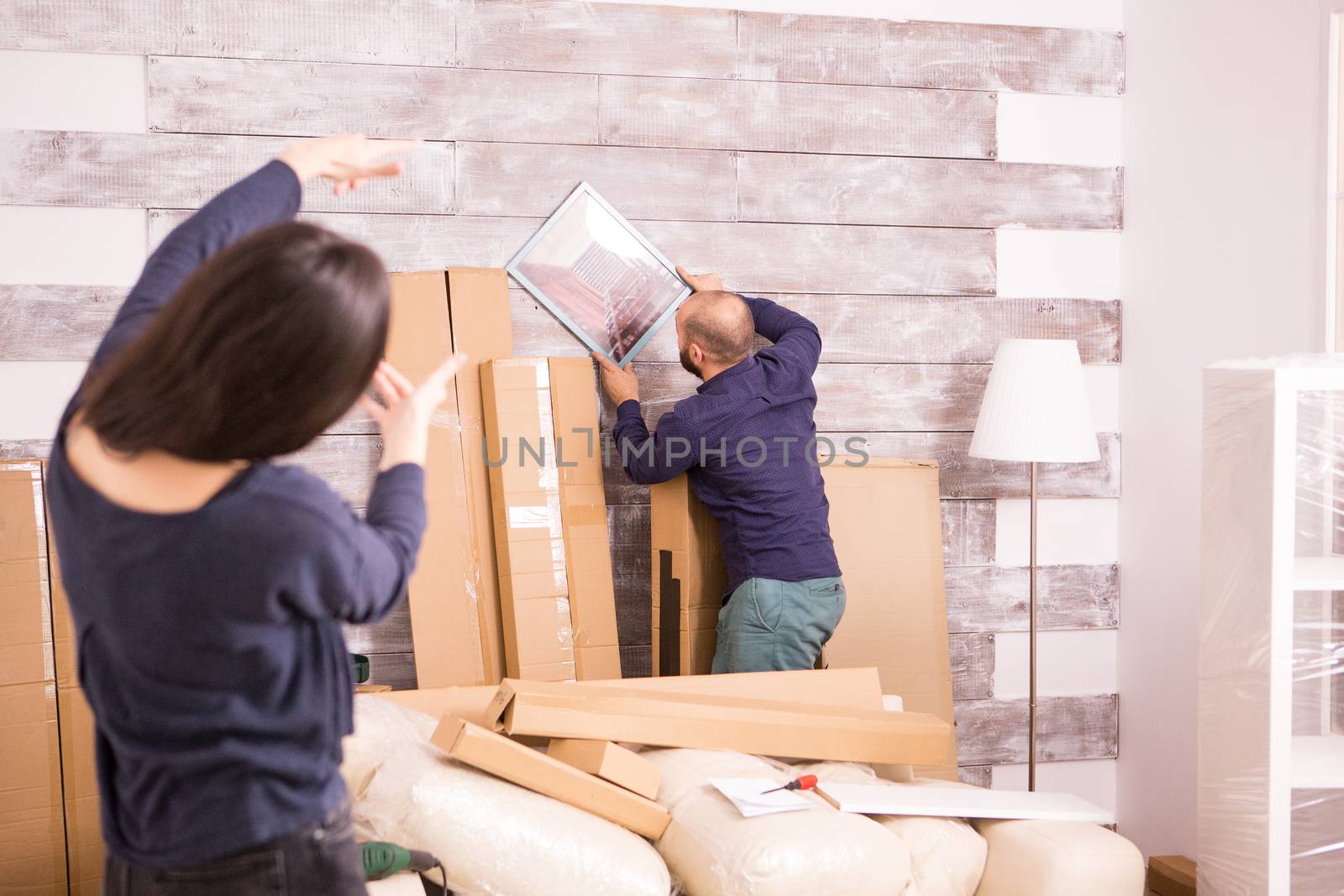 Girlfriend helping her boyfriend to hang picture on the wall of their new apartment.