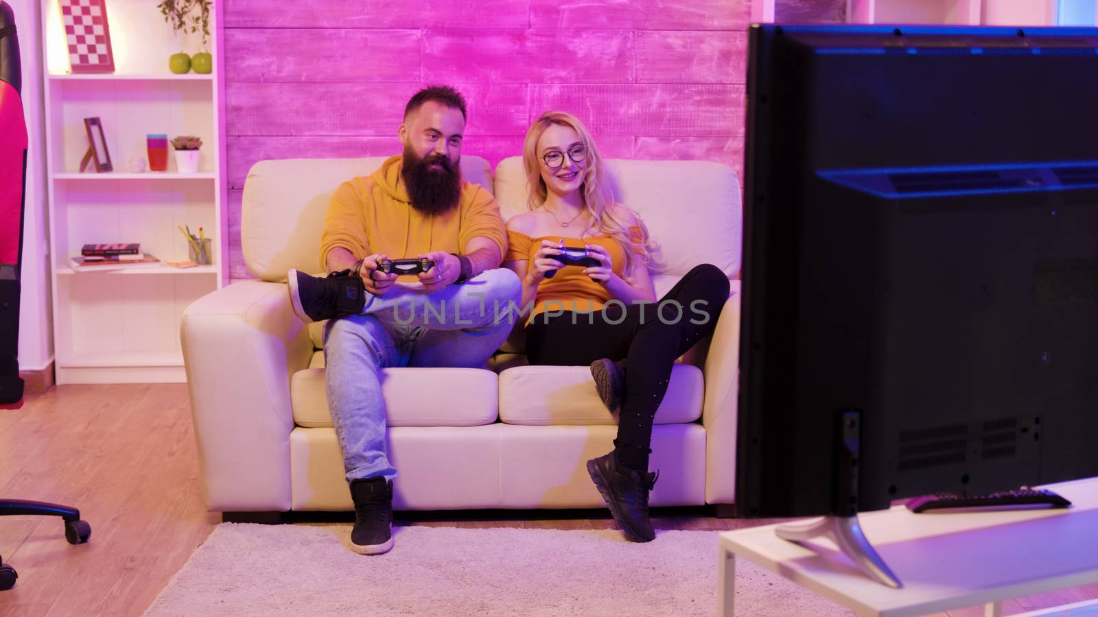 Revealing footage of beautiful young couple playing together video games on a big screen TV using wireless controllers.