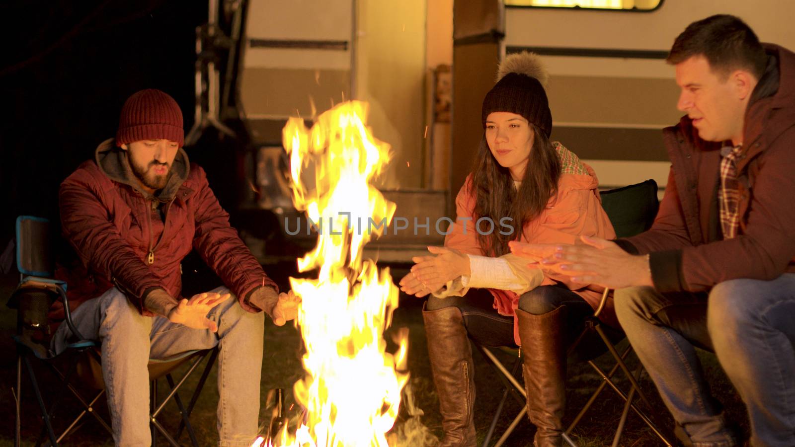 Handheld footage of friends warming their hand at camp fire in a cold autumn night. Retro camper van. Tourists enjoying fresh air.